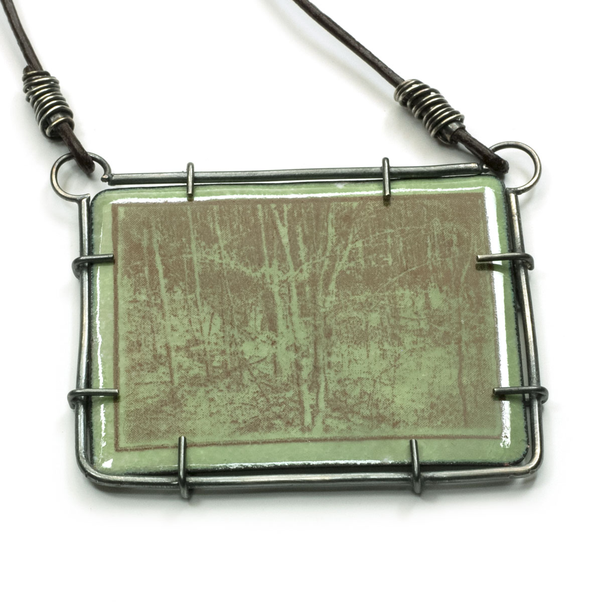 Green enamel pendant with a brown trees overlayed and a patinaed sterling silver setting on a brown leather cord.